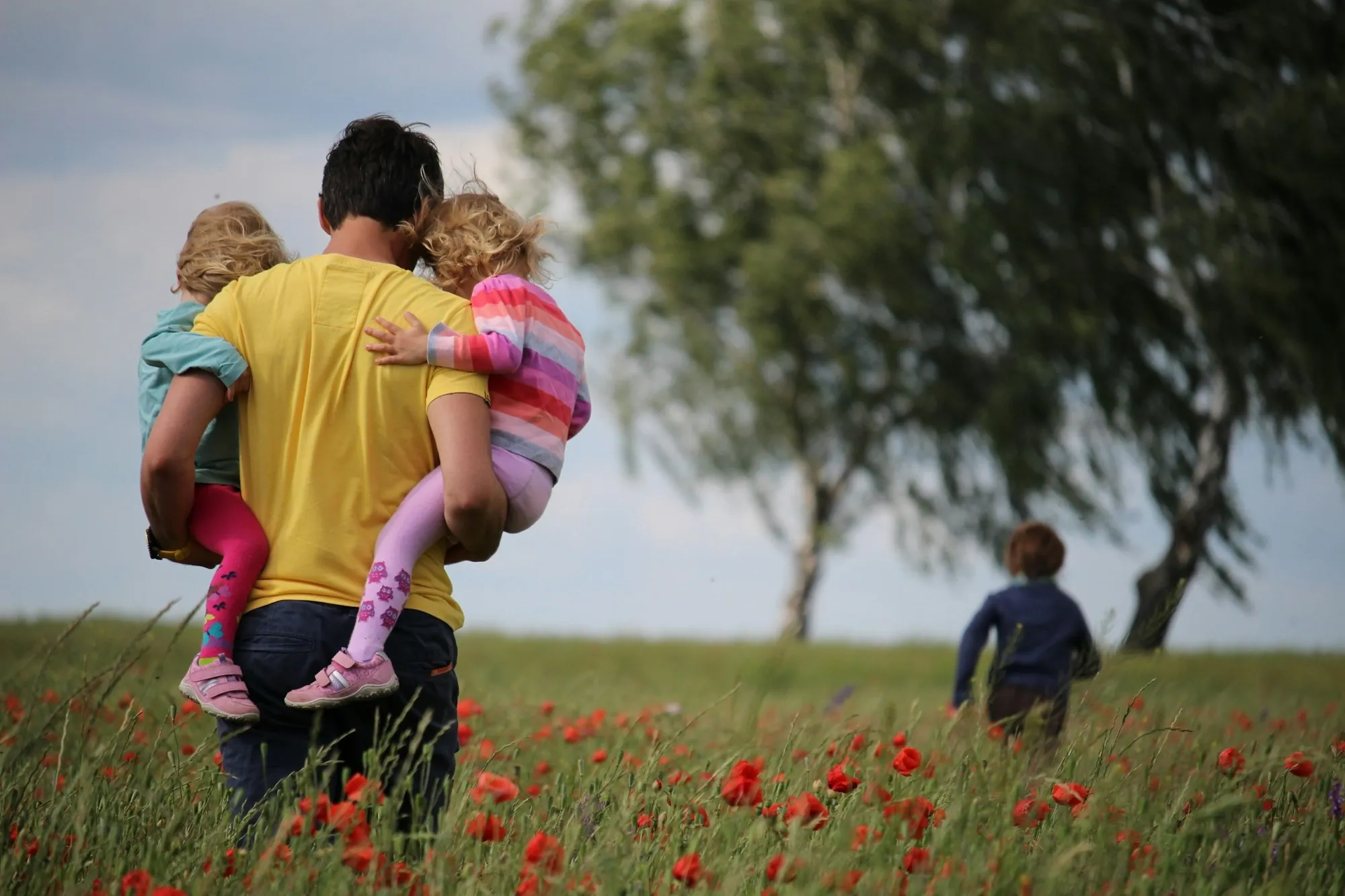 Father carrying two children through a field of poppies