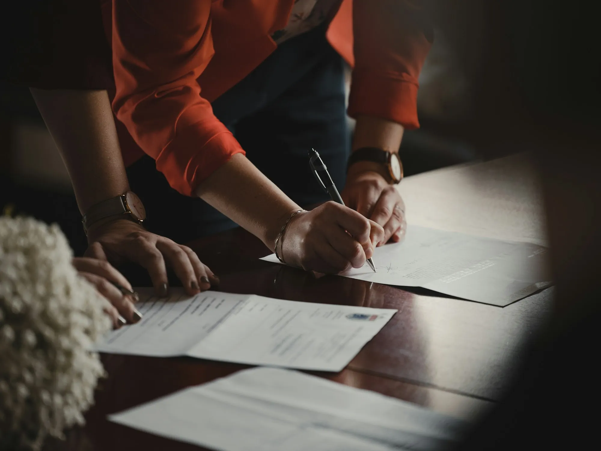Hands signing a document at a wooden table